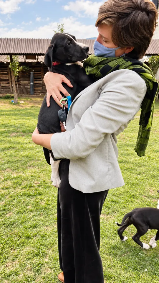 Una mujer sostiene a su cachorro negro en el jardín.